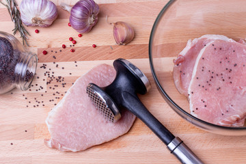 Raw pork schnitzel with meat tenderizer on wooden board