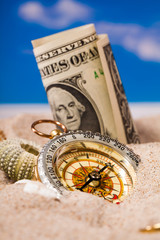 Sea shells compass and dollar money on  sand