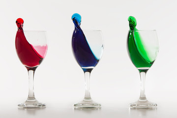 Three wine glasses with colour water spill on white background w