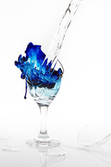 Blue water spill from a broken wine glass on white background