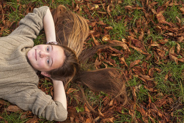 Сute girl lying on fallen leaves in autumn park.
