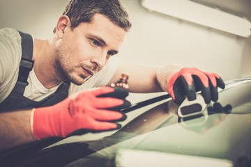 Worker on a car wash applying anti rain coating on a windshield