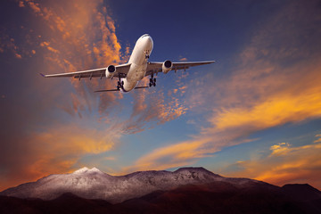 Fototapeta na wymiar passenger plane flying above rock mountain against beautiful dus
