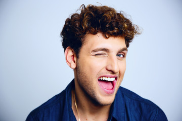 Cheerful young man winking over blue background
