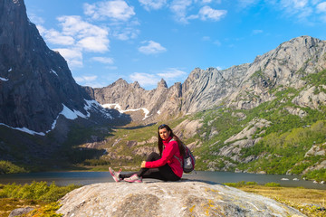 Naklejka na ściany i meble Young tourist woman is sitting on stone near mountain lake