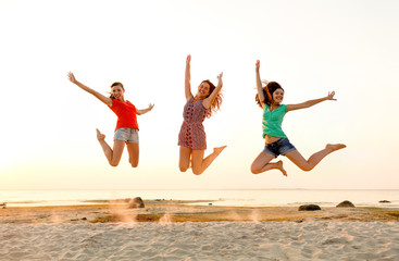 smiling teen girls jumping on beach