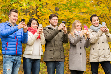 smiling friends with smartphones in city park