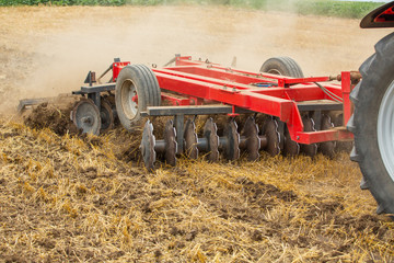 Naklejka premium Tractor cultivating wheat stubble field, crop residue.