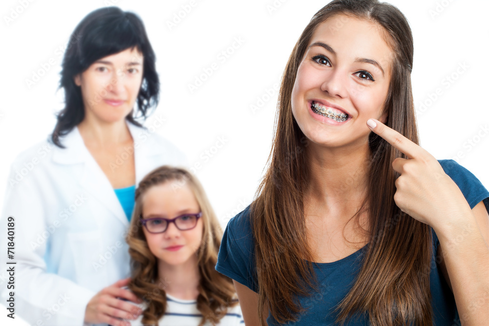 Wall mural Teen girl pointing at dental barces with doctor in background.