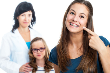 Teen girl pointing at dental barces with doctor in background.