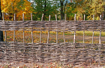 Wicker fence against the backdrop of autumn trees