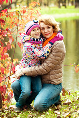 girl and mother are hiding behind a tree in the autumn park