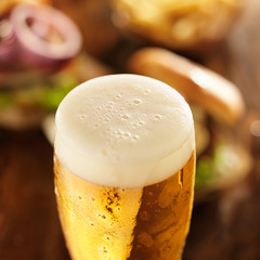 foamy cold glass of beer with burgers in background