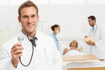 Doctor using stethoscope with colleagues and patient behind