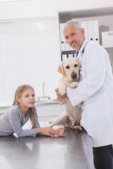 Smiling vet examining a dog with its owner