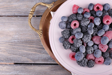 Iced berries on plate, on color wooden background