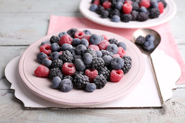 Iced berries on plate, on color wooden background