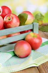 Sweet apples in wooden box on table on bright background