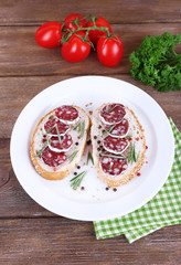 Sandwiches with salami on plate on napkin on wooden background