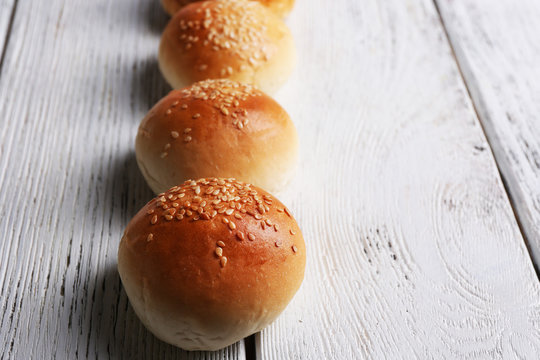 Tasty buns with sesame on color wooden background