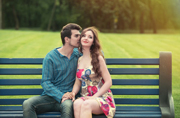 Naklejka premium Young couple in love sitting together on the bench in the park
