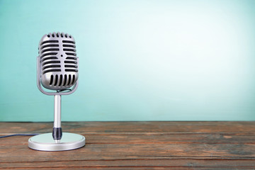 Old metal microphone on wooden table on light blue background