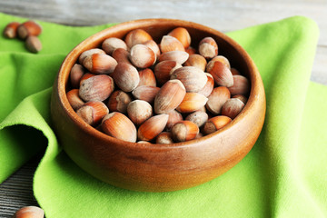 Hazelnuts in wooden bowl, on napkin on wooden background