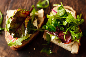 Two sandwiches with basil and rocket salad on a board