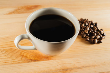 white cup of coffee on a wooden background and coffee beans