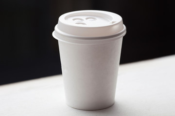 Disposable coffee cup on windowsill with blurred city in background.