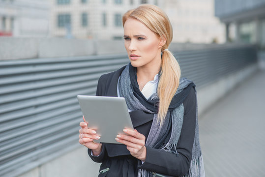 Woman holding a tablet standing thinking