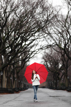 Girl with red umbrella walking in park in fall