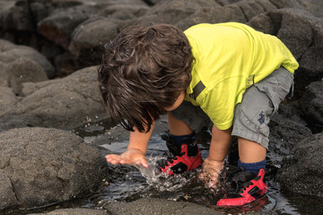 Toddler boy plays with water on lava rock