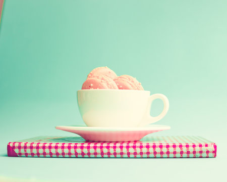 Pink macaroons in a white tea cup over book