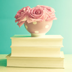 Pink roses in a vintage polka dots bowl over a pile of books