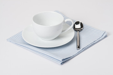 Cup, Plate And Spoon On Folded Gingham Cotton Napkin. White Back