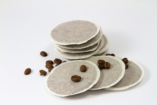 Neun Kaffeepads mit einzelnen Kaffeebohnen auf weißem Grund