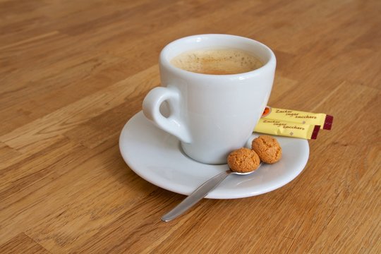 Kaffeetasse mit Zuckertütchen und Gebäck auf brauner Tischplatte