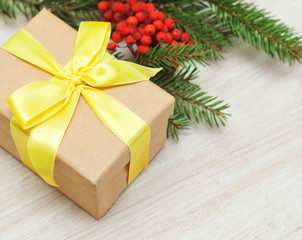 beige gift box with yellow ribbon on fir branches background