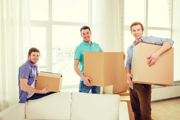 Fototapeta na wymiar smiling male friends carrying boxes at new place