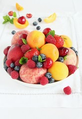 Plate with seasonal fruits and berries on white background.