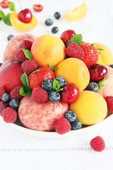 Plate with seasonal fruits and berries on white background.