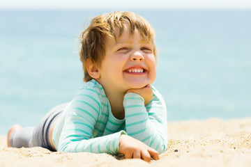 Fototapeta na wymiar laughing three-year girl laying on beach