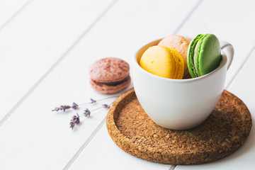 Coloured macarons in cup on white wooden background