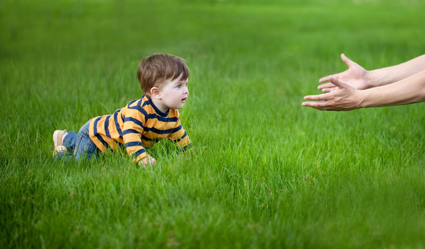 son crawling in her father's hands on green grass