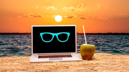 Laptop on the beach wearing sanglass and drinking coconuts water