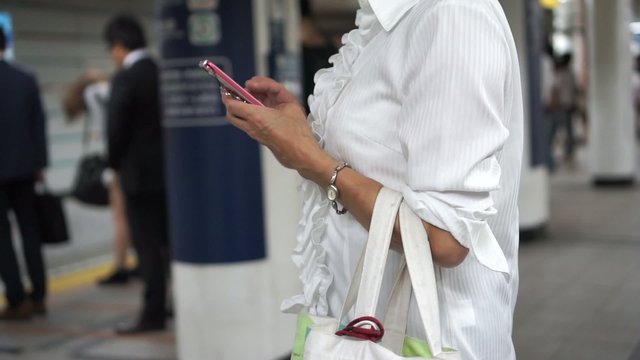 駅のホームでスマートフォンを操作する女性