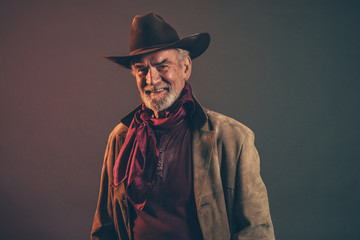 Smiling old rough western cowboy with gray beard and brown hat.