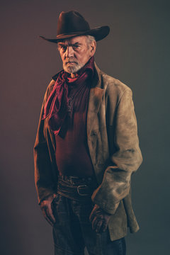 Old rough western cowboy with gray beard and brown hat. Low key