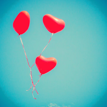 Three red heart-shaped balloons flying away